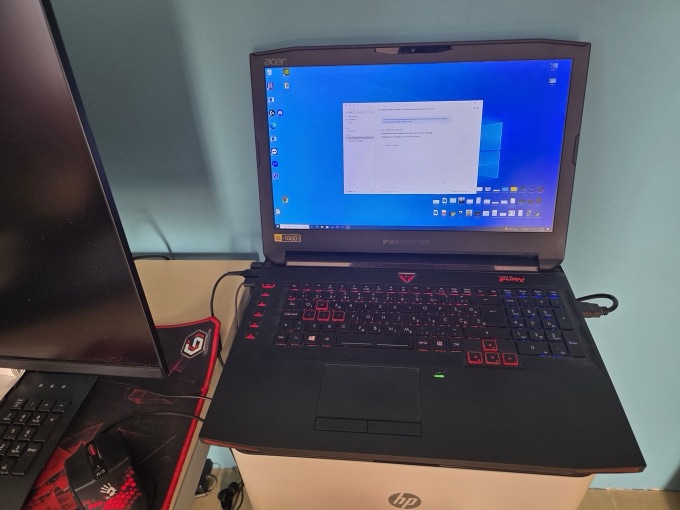 A 2018-era gaming laptop with a red and blue split-zone keyboard backlight, lid open, beside an external monitor and gaming mouse.